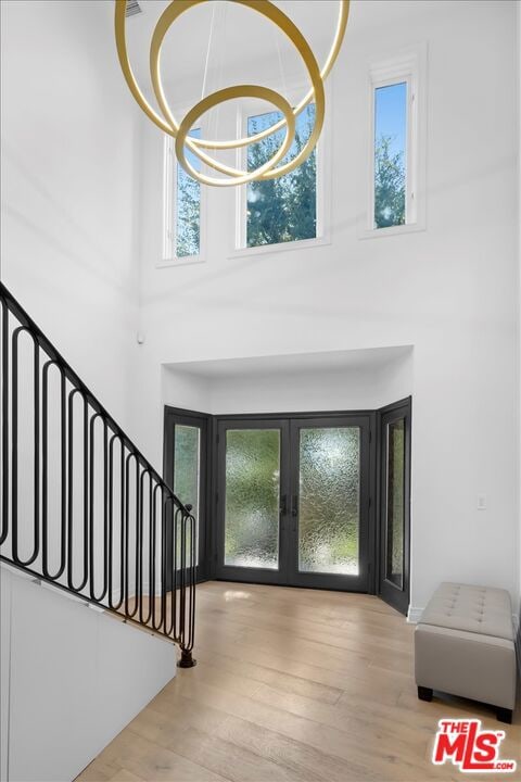 foyer entrance with french doors, light hardwood / wood-style floors, a notable chandelier, and a high ceiling