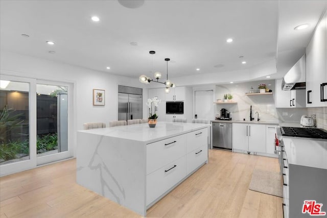 kitchen with hanging light fixtures, white cabinetry, light wood-type flooring, stainless steel appliances, and a center island