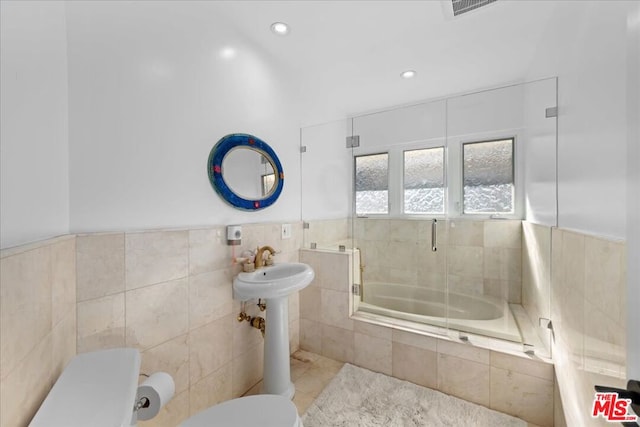 bathroom featuring toilet, combined bath / shower with glass door, tile patterned floors, and tile walls