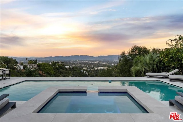 pool at dusk with an in ground hot tub and a mountain view