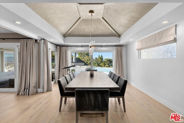 dining room with a raised ceiling, lofted ceiling, and light hardwood / wood-style flooring