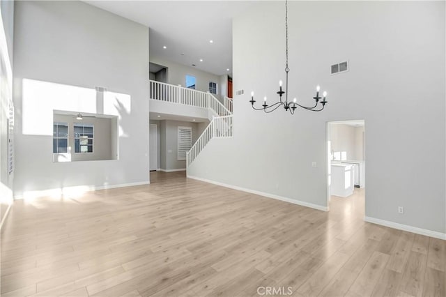 unfurnished living room featuring ceiling fan with notable chandelier, light hardwood / wood-style floors, and a high ceiling