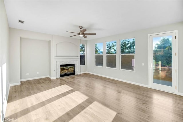 unfurnished living room featuring ceiling fan, a wealth of natural light, a high end fireplace, and light wood-type flooring