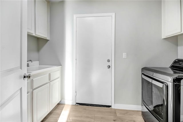 clothes washing area with cabinets, light hardwood / wood-style flooring, washer and clothes dryer, and sink