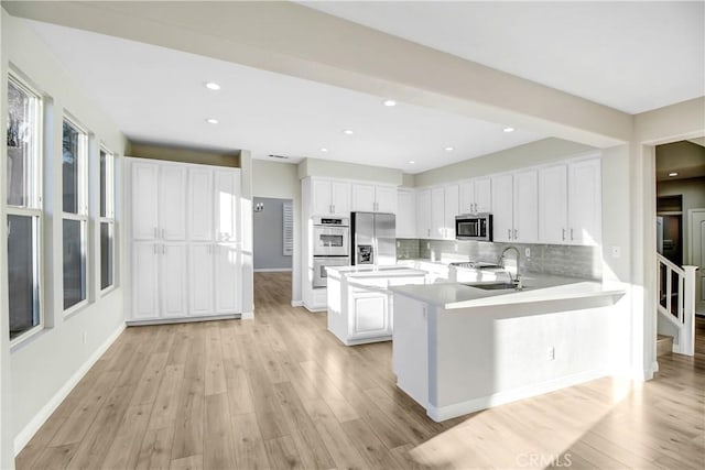 kitchen featuring kitchen peninsula, stainless steel appliances, white cabinetry, and light hardwood / wood-style floors