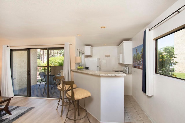 kitchen with light wood-type flooring, white appliances, kitchen peninsula, a kitchen bar, and white cabinetry