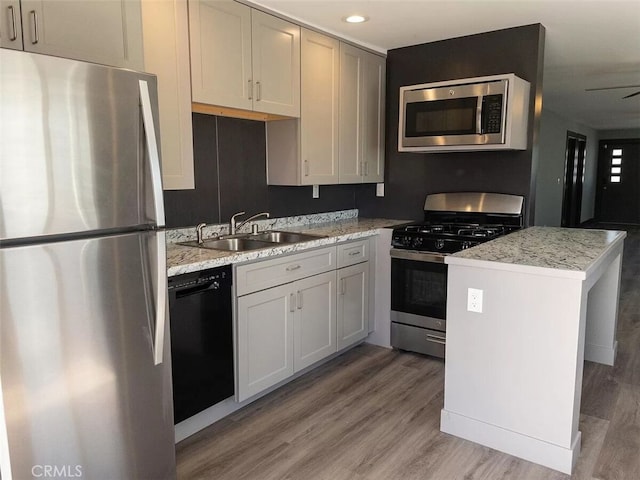 kitchen featuring wood-type flooring, a kitchen island, sink, light stone countertops, and appliances with stainless steel finishes