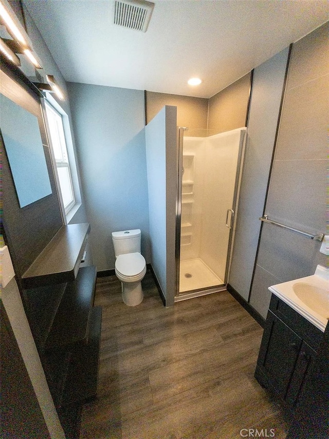 bathroom with hardwood / wood-style flooring, toilet, vanity, and a shower with shower door