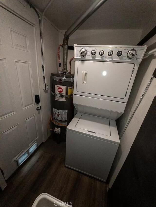 clothes washing area featuring dark wood-type flooring, stacked washer / drying machine, and secured water heater