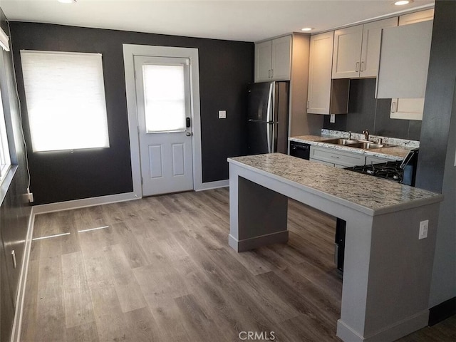 kitchen featuring light wood-type flooring, sink, stainless steel refrigerator, light stone countertops, and black range oven