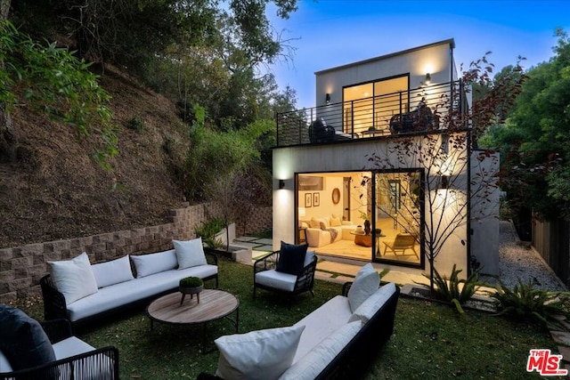 back house at dusk with an outdoor living space and a balcony