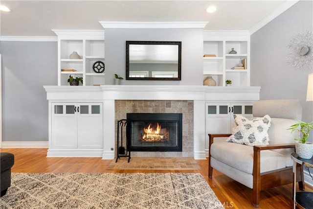 living area with hardwood / wood-style flooring, crown molding, and a tiled fireplace