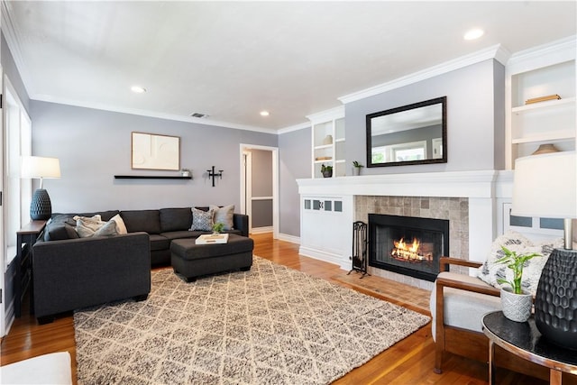 living room featuring hardwood / wood-style floors, a tile fireplace, and crown molding