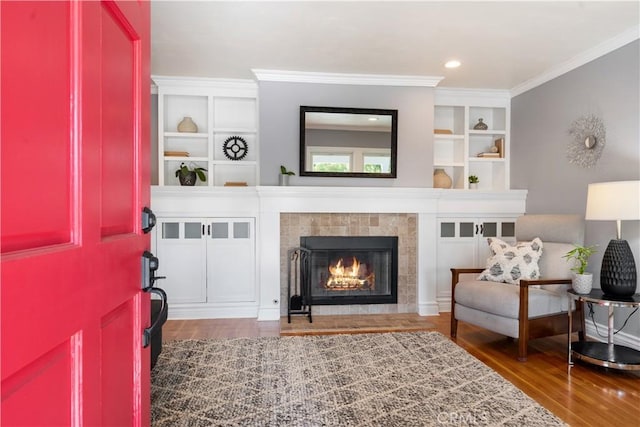 living area with a fireplace, built in shelves, dark hardwood / wood-style floors, and ornamental molding