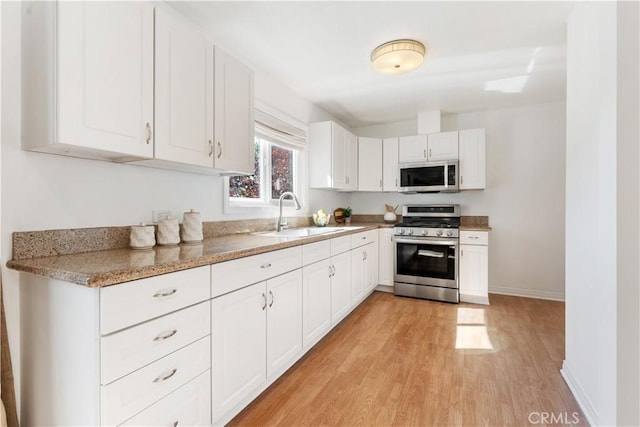 kitchen featuring sink, white cabinetry, light hardwood / wood-style flooring, light stone countertops, and stainless steel appliances