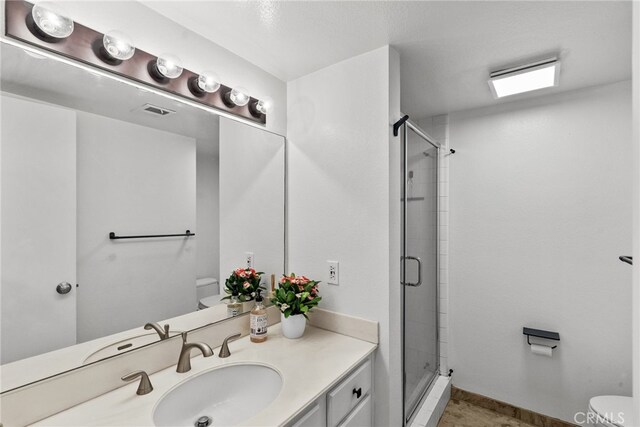 bathroom with vanity, toilet, a shower with shower door, and a textured ceiling