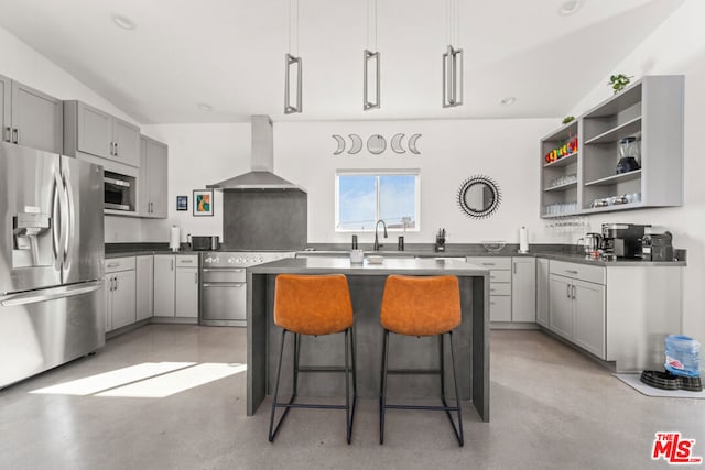 kitchen with a center island, stainless steel appliances, wall chimney exhaust hood, vaulted ceiling, and a kitchen breakfast bar