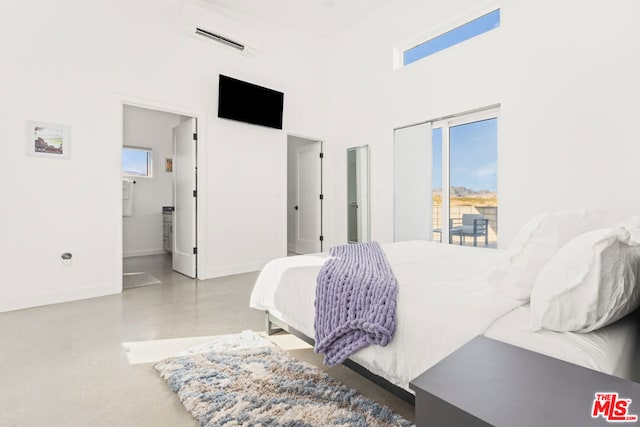 bedroom featuring a high ceiling, an AC wall unit, ensuite bathroom, concrete floors, and access to outside