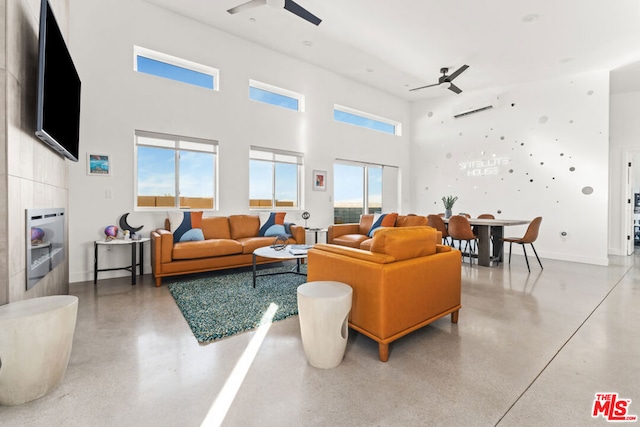 living room with a fireplace, a wealth of natural light, a towering ceiling, and concrete flooring