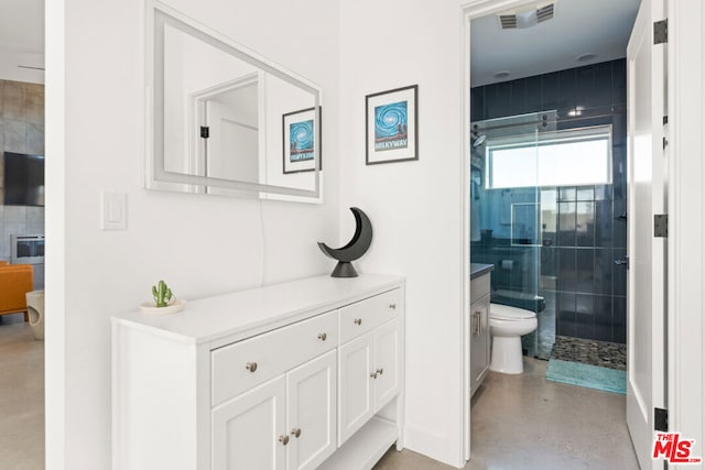 bathroom with concrete floors, a tile shower, vanity, and toilet