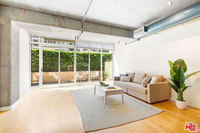 living room featuring an AC wall unit, light hardwood / wood-style flooring, and a wall of windows