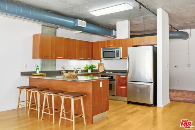 kitchen featuring sink, light hardwood / wood-style flooring, kitchen peninsula, a breakfast bar, and appliances with stainless steel finishes