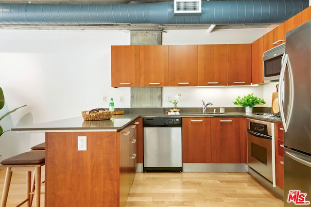 kitchen with kitchen peninsula, appliances with stainless steel finishes, a kitchen breakfast bar, sink, and light hardwood / wood-style flooring