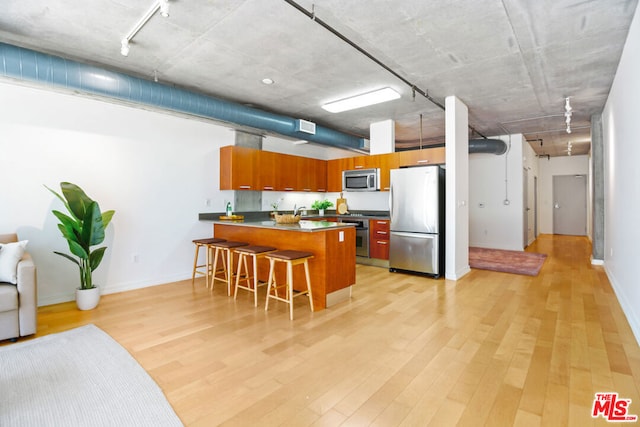 kitchen featuring kitchen peninsula, appliances with stainless steel finishes, rail lighting, a kitchen breakfast bar, and light hardwood / wood-style floors