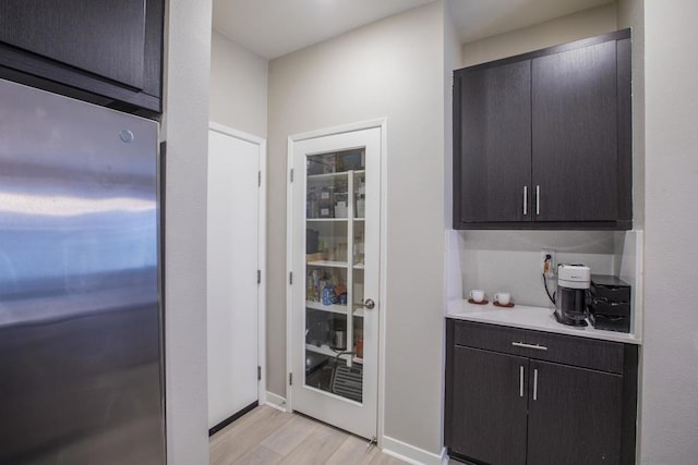 bar featuring dark brown cabinetry, stainless steel fridge, and light hardwood / wood-style floors