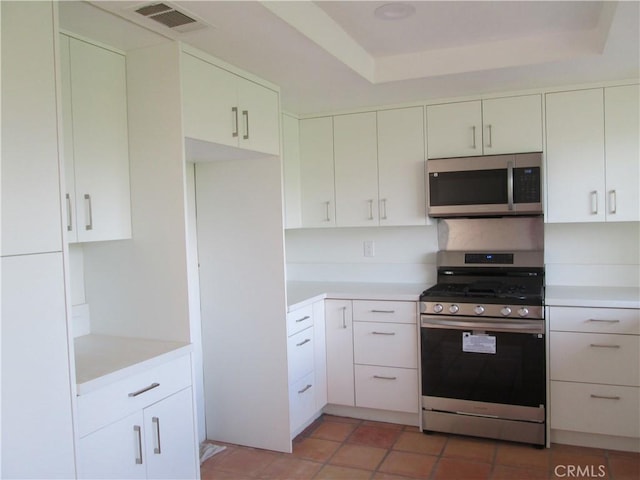 kitchen with a raised ceiling, white cabinetry, appliances with stainless steel finishes, and tile patterned flooring