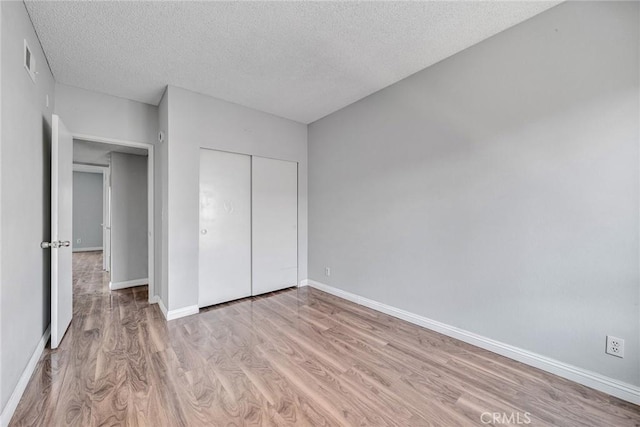 unfurnished bedroom with light wood-type flooring, a closet, and a textured ceiling