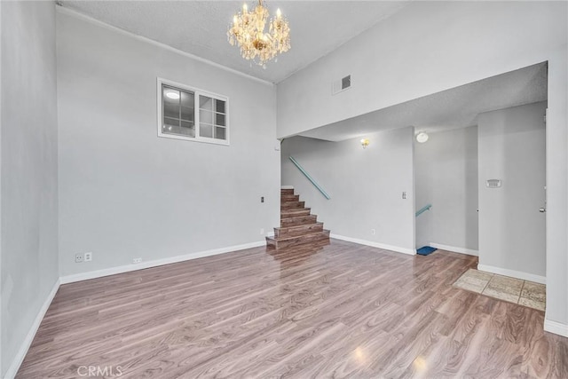 unfurnished living room with light wood-type flooring, an inviting chandelier, and a high ceiling