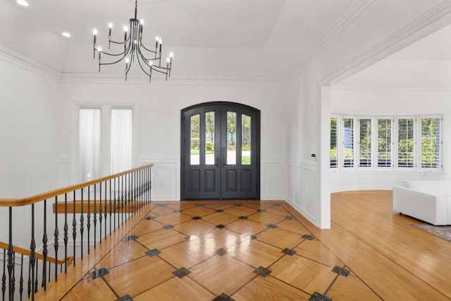 entrance foyer featuring french doors, wood-type flooring, a chandelier, ornamental molding, and a tray ceiling