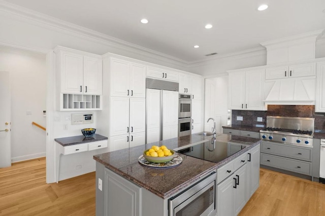 kitchen with built in appliances, a kitchen island with sink, and white cabinets