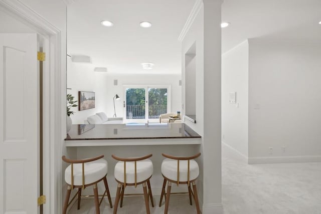 kitchen featuring crown molding, a breakfast bar area, light colored carpet, and kitchen peninsula