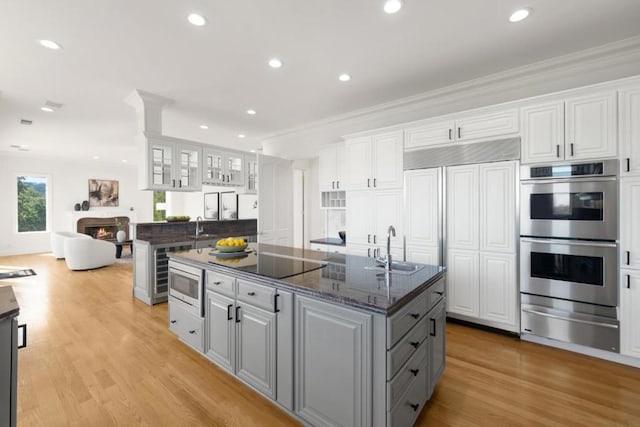 kitchen with white cabinetry, dark stone counters, built in appliances, and sink