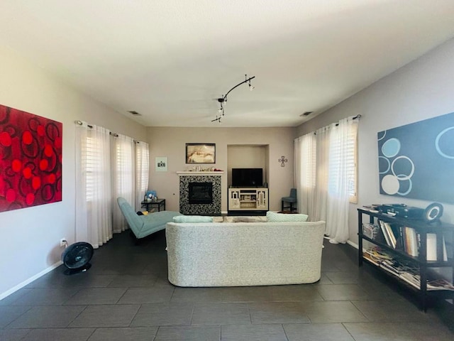 living room with track lighting, dark tile patterned floors, a wealth of natural light, and a tile fireplace