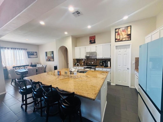 kitchen featuring a center island with sink, sink, light stone countertops, white cabinets, and white fridge