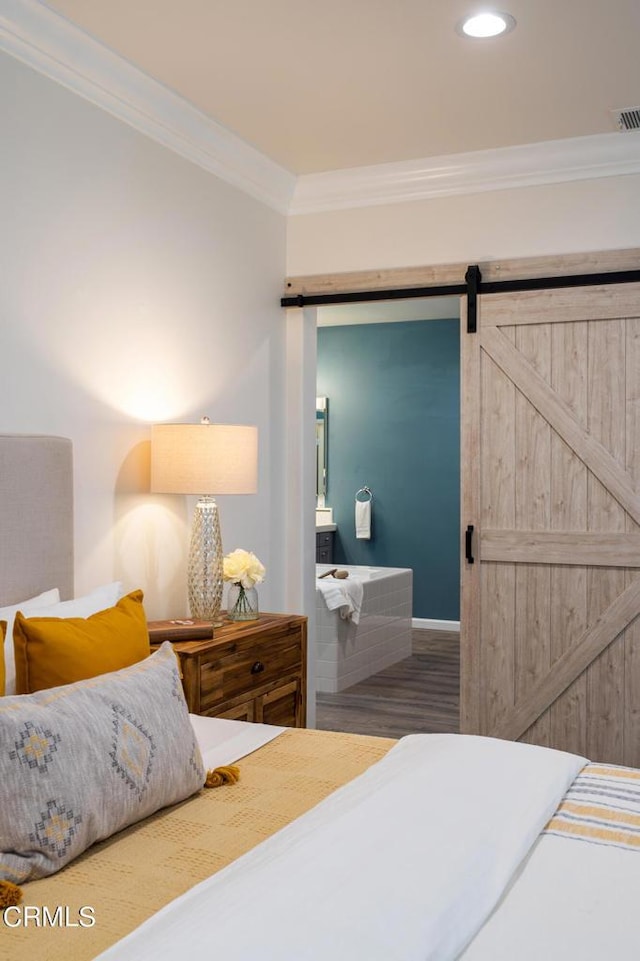 bedroom with a barn door, hardwood / wood-style floors, and ornamental molding