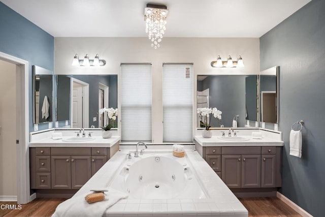 bathroom featuring vanity, wood-type flooring, tiled tub, and a chandelier