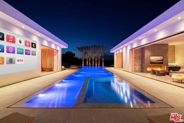 pool at night featuring a patio area