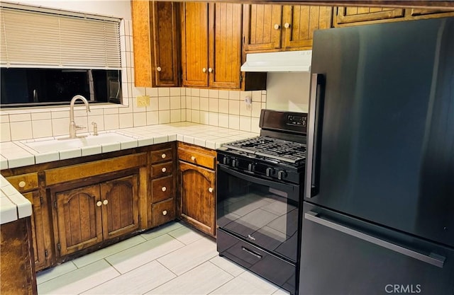 kitchen featuring tile countertops, stainless steel fridge, sink, and black range with gas cooktop