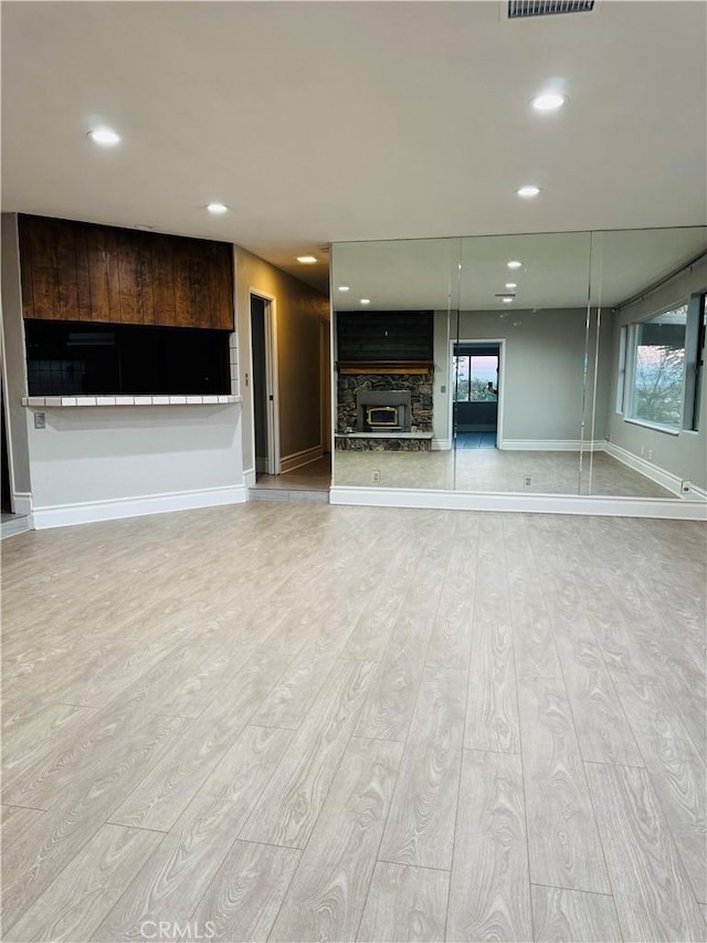 unfurnished living room featuring light wood-type flooring and a stone fireplace