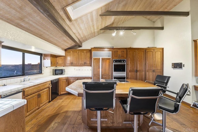 kitchen featuring a breakfast bar area, paneled built in fridge, dishwasher, lofted ceiling with skylight, and a kitchen island