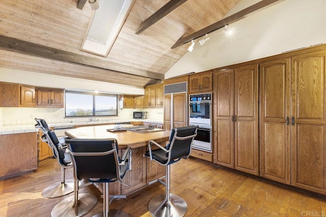 kitchen with multiple ovens, a kitchen bar, wooden ceiling, light wood-type flooring, and a center island