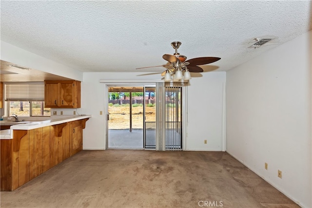 kitchen featuring ceiling fan, light colored carpet, sink, kitchen peninsula, and a textured ceiling