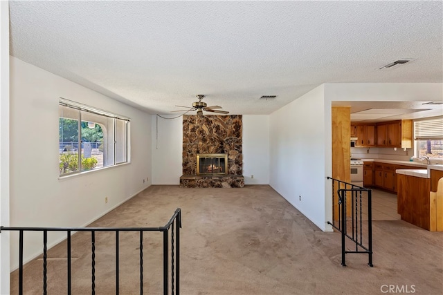 living room with light carpet, a stone fireplace, a textured ceiling, and ceiling fan