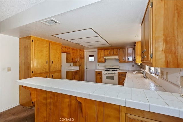 kitchen featuring tile counters, sink, gas range gas stove, and kitchen peninsula