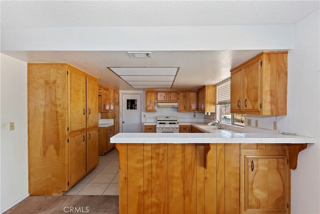 kitchen with gas range gas stove, kitchen peninsula, light tile patterned floors, and a textured ceiling