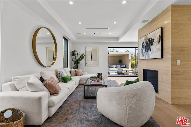 living room featuring wood-type flooring, a large fireplace, a raised ceiling, and a wealth of natural light